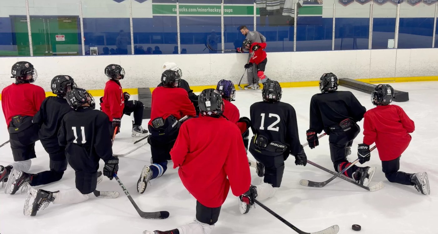 Falcons players kneel on the ice in a semicircle listening to a coach during a team practice